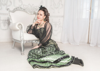beautiful young smiling woman wearing green medieval vintage victorian style dress sitting on the fl