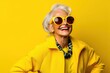 Happy senior woman in colorful yellow outfit, cool sunglasses, laughing and having fun in fashion studio