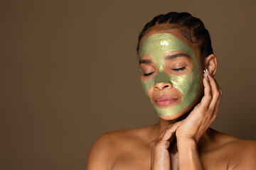 Sensual african american middle aged woman with green peel-off mask on her face posing on brown background, copy space