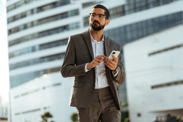 Poster - Young businessman walking around the city using his smartphone