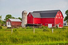 Red Barn And Dirty White Silo On Farm With Wood Poles And Wire Fencing