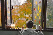 A Cute Boy Wrapped In A Blanket Drink Hot Tea And Looks Out The Open Window At The Wonderful Autumn Nature. Autumn Home Decor. Cozy Fall Mood. Thanksgiving. Halloween.