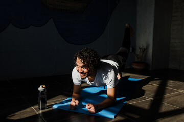 Wall Mural - Young latin man practicing yoga and fitness with online training on laptop at home in Mexico Latin America, hispanic people