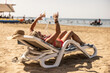 © weyo - A woman lying on a beach chair by the sea pours cold water on herself during hot summer days
