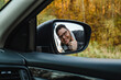 © phpetrunina14 - A smiling man in the side mirror of the car shows a big stick up behind the autumn forest