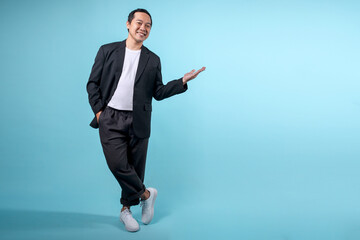 Asian businessman wearing semi-formal suit and presenting gesture to empty space on blue background