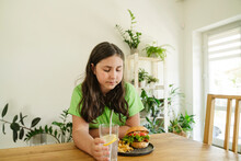 Girl Staring At Burger On Table At Home