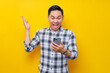 © Bangun Stock Photo - Excited young Asian man wearing a white checkered shirt reading messages on his mobile phone and emotionally reacting to online news isolated on yellow background. People Lifestyle Concept