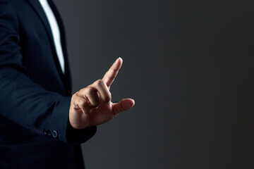 Businessman is pointing a finger against dark background.