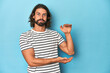 © Asier - Bearded man in a striped shirt, blue backdrop shocked and amazed holding a copy space between hands.