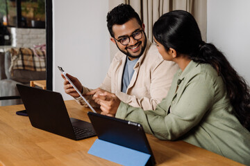 Wall Mural - Two business people reading financial report while sitting at table with laptop and tablet