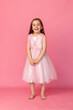 © Irina Mikhailichenko - Cute happy laughing little girl in a pink princess dress posing on pink background. Kids Birthday party celebration concept. Happy Birthday banner with copy space. Studio shot.