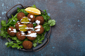 plate of fried falafel balls served with fresh green cilantro and lemon top view on rustic concrete 