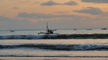 Two Fishermen Run Their Boat Away From The Shore Of Pangandaran At Sunset. Many Fishing Boats Were Seen Sailing In The Distance. Taken With Handheld, Slow Motion, And Telephoto Lens.