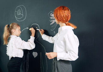 Wall Mural - Girl, student of primary school standing at chalkboard with teacher and drawing human representation. Anatomy lessons. Concept of school, education, childhood, knowledge, lifestyle