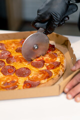 man pizza chef cuts pizza lying in a delivery box with a pizza knife in the kitchen of a pizzeria 