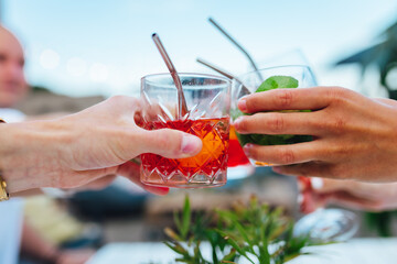 Wall Mural - Group of friends toasting multicolored cocktails at the summer terrace