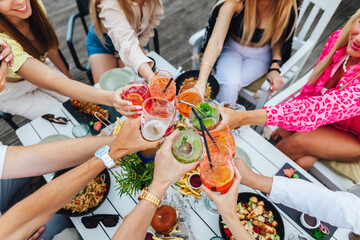 Group of friends toasting multicolored cocktails at the summer terrace