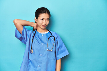 Asian nurse with stethoscope, medical studio shot, touching back of head, thinking and making a choice.