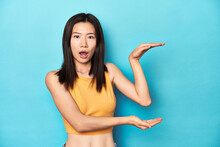 Asian Woman In Summer Yellow Top, Studio Setup, Shocked And Amazed Holding A Copy Space Between Hands.