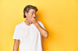 © Asier - Middle-aged man posing on a yellow backdrop thoughtful looking to a copy space covering mouth with hand.