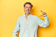 © Asier - Middle-aged man posing on a yellow backdrop holding something little with forefingers, smiling and confident.