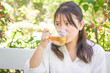 © Rizky - A beautiful asian woman in white is sipping a glass of hot tea in the morning with bokeh garden backgrounds. Herbal drinks, Alternative medicine, Healthy food, Relaxation, Leisure activity concept
