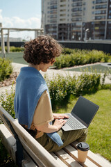 Poster - Side view of young brunette businesswoman with laptop on knees sitting on bench and watching online video or looking through news