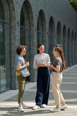 Aufkleber - Three young businesswomen in casualwear standing in front of camera and having discussion of working points at meeting in urban environment