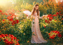 Portrait Vintage Lady Fantasy Girl Medieval Princess Holding Fan In Hands Waving Enjoying Wind Green Summer Nature Garden Red Roses Magic Sun Light. Young Woman Queen Old Style White Pink Long Dress
