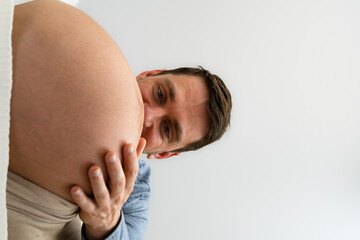 Wall Mural - Happy father looking closely  on naked baby belly of standing expectant mother. Side view. White background. Bright shot.