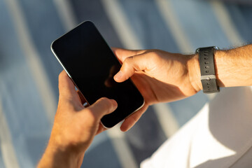 Poster - Cropped of male hands using smartphone, blurred outdoor background
