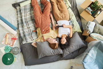 Wall Mural - High angle of two young women having rest on the floor of living room while lying on checkered plaid and greyr pillows and watching video