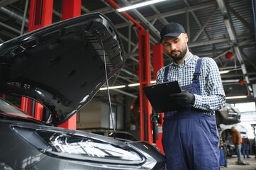 Leinwandbilder - Smiling mechanic writing on clipboard at the repair garage