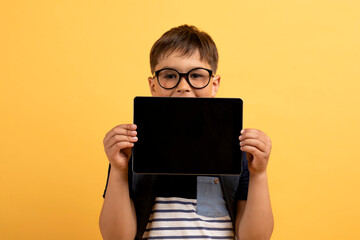 Happy school kid showing digital tablet with blank screen