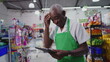 © Marco - Confused senior worker of supermarket using technology feeling frustration, scratching forehead while holding tablet device
