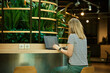 © Lazy_Bear - Woman using laptop in coworking with green plants. Female freelancer typing on laptop keyboard. Online work in cafe