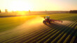 A tractor sprays an agricultural field with fertilizer on a sunset evening. drone view. Generative AI