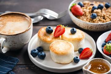 Wall Mural - Syrniki, cottage cheese fritters served with berries, honey and cup of cappuccino coffee. Russian breakfast