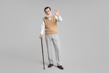 Wall Mural - Senior man with walking cane waving on light gray background