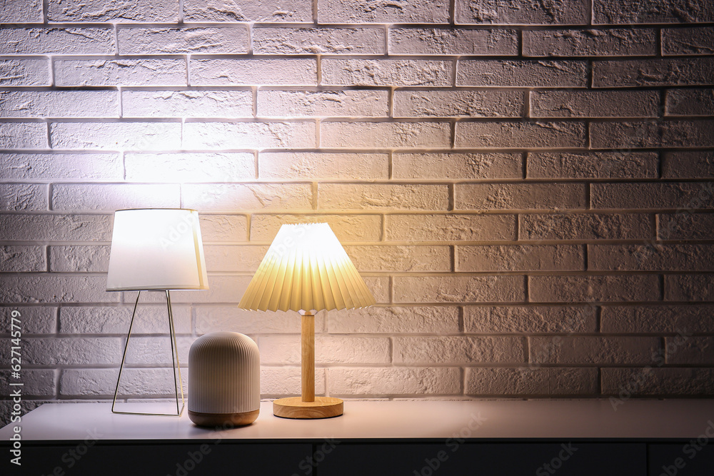 Different glowing lamps on table near white brick wall in dark room
