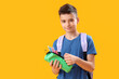 Little schoolboy with pencil case on orange background