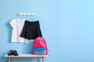 Table with backpack, shoes and stylish school uniform hanging on blue wall in room