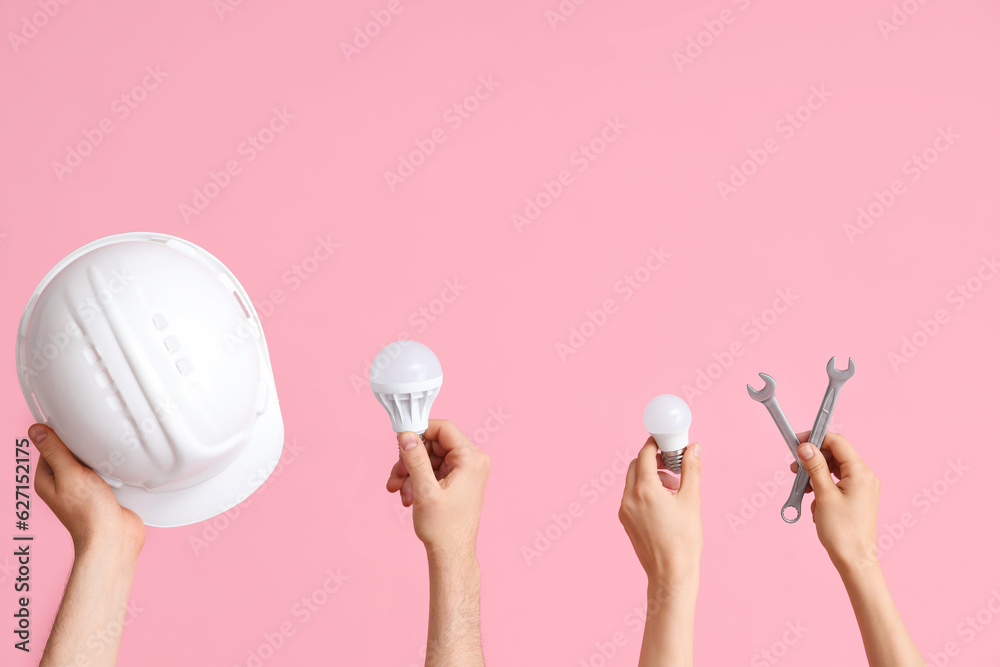 Electrician hands with hardhat, light bulbs and wrenches on pink background