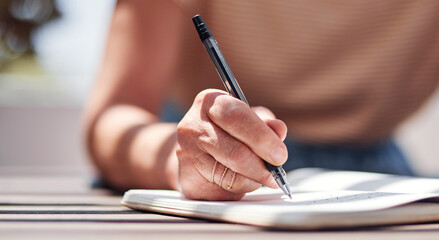 Hand, writing and book with a woman author sitting outdoor in summer for inspiration as a writer. Idea, planning and notebook with a female person using a pen to write in her journal or diary outside