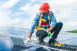 © chokniti - African American engineer maintaining solar cell panels on factory building rooftop. Technician working outdoor on ecological solar farm construction. Renewable clean energy technology concept