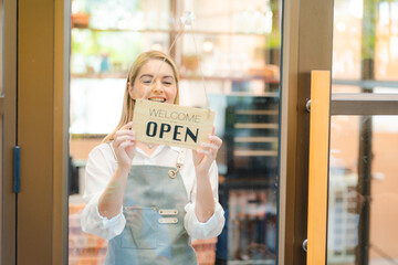 Hand of coffee shop staff woman wearing apron turning open sign board on glass door in modern cafe, morning of hotel service or restaurant retail store, small business owner in food and drink concept