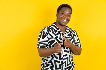 Young latin man wearing printed shirt over yellow background pointing fingers to camera with happy and funny face. Good energy and vibes.