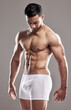 © Alexis Scholtz/peopleimages.com - Man, underwear model and muscle care with strong chest, abs and body with wellness in studio. Bodybuilder, exercise and healthy male person with gray background and muscles from fitness and workout