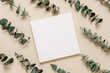 Aesthetic blank paper mockup card with eucalyptus leaves background, top view. Empty card template for wedding, greeting, invitation and branding, logo and design, bohemian style.